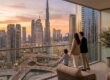 Une famille observant le panorama urbain de Dubaï depuis un balcon luxueux au coucher du soleil.