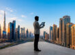 Un homme d'affaires consulte une tablette face à la ligne d'horizon de Dubaï au coucher du soleil.