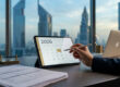 Une personne utilise un stylet sur une tablette affichant un calendrier 2026 dans un bureau avec vue sur Dubaï.