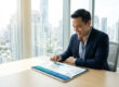 Entrepreneur souriant consultant un tableau de bord financier sur tablette dans un bureau avec vue sur la ville.