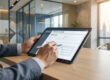 Personne en costume remplissant un formulaire de déclaration UBO sur une tablette dans un bureau moderne.