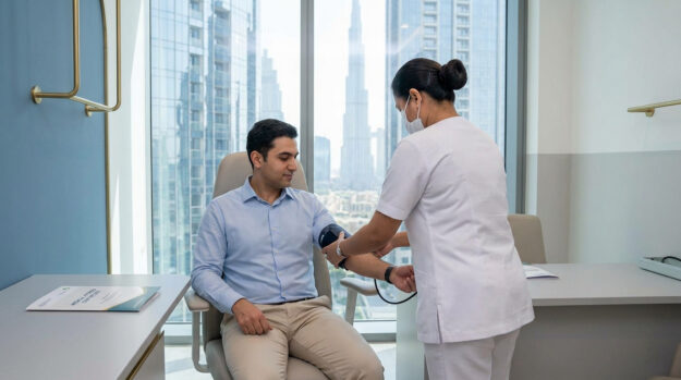 Une infirmière prend la tension artérielle d'un homme dans un cabinet médical moderne avec vue sur Dubaï.