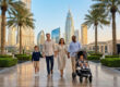 Une famille heureuse se promène avec son enfant en poussette dans un parc moderne avec les gratte-ciels de Dubaï en arrière.
