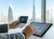 Une personne tenant un passeport émirati et utilisant une tablette numérique avec une vue sur les gratte-ciels de Dubaï.
