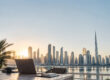 Un ordinateur portable sur une table face au panorama urbain de Dubaï au lever du soleil.