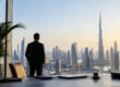 Un homme d'affaires en costume regarde la skyline de Dubaï et le Burj Khalifa depuis un bureau panoramique.