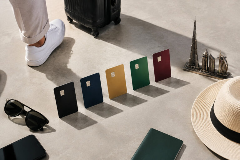 Cinq cartes bancaires colorées alignées au sol avec des accessoires de voyage et des miniatures de monuments de Dubaï.