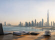 Bureau avec ordinateur, documents et tasse de café face à la skyline de Dubaï au coucher du soleil.