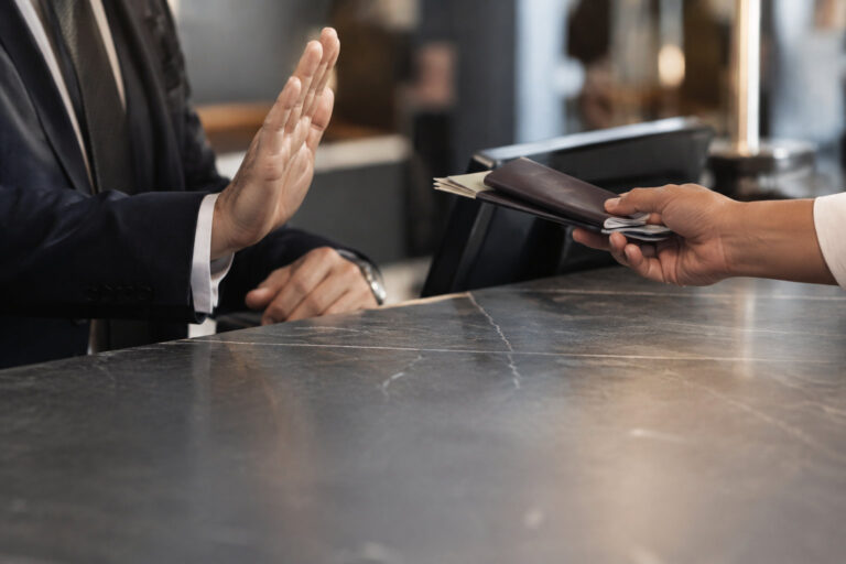 Un banquier en costume fait un geste de refus de la main à une personne présentant ses documents d'identité.
