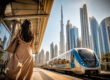Une femme attend le métro à Dubaï avec la skyline et le Burj Khalifa en arrière-plan.