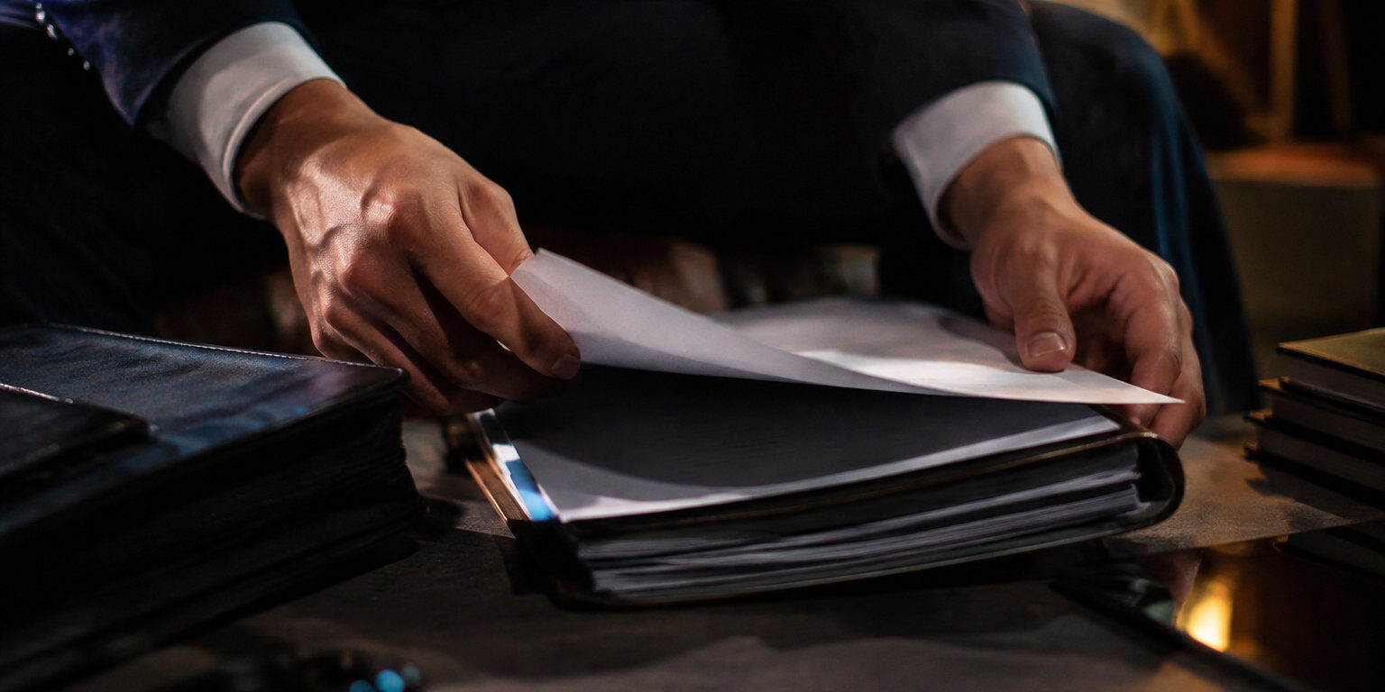 Procédure de transfert de zone franche à Dubaï Gros plan sur les mains d'un homme en costume feuilletant des documents officiels sur un bureau sombre.