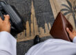 Un entrepreneur en kandoura tient une valise et une pochette en cuir sur un sol gravé d'une silhouette de Dubaï.