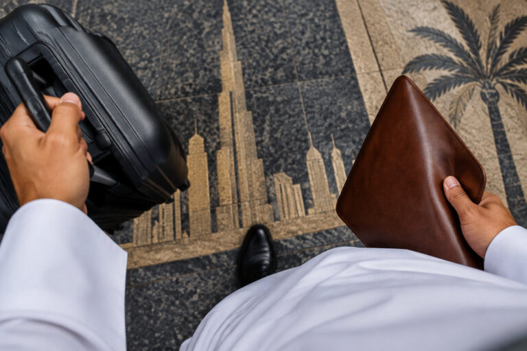 Un entrepreneur en kandoura tient une valise et une pochette en cuir sur un sol gravé d'une silhouette de Dubaï.