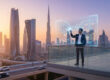Un homme d'affaires sur un balcon à Dubaï manipulant une interface numérique de trading et de conformité réglementaire.