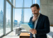 Un homme d'affaires consulte des données financières sur une tablette numérique avec la skyline de Dubaï en arrière-plan.